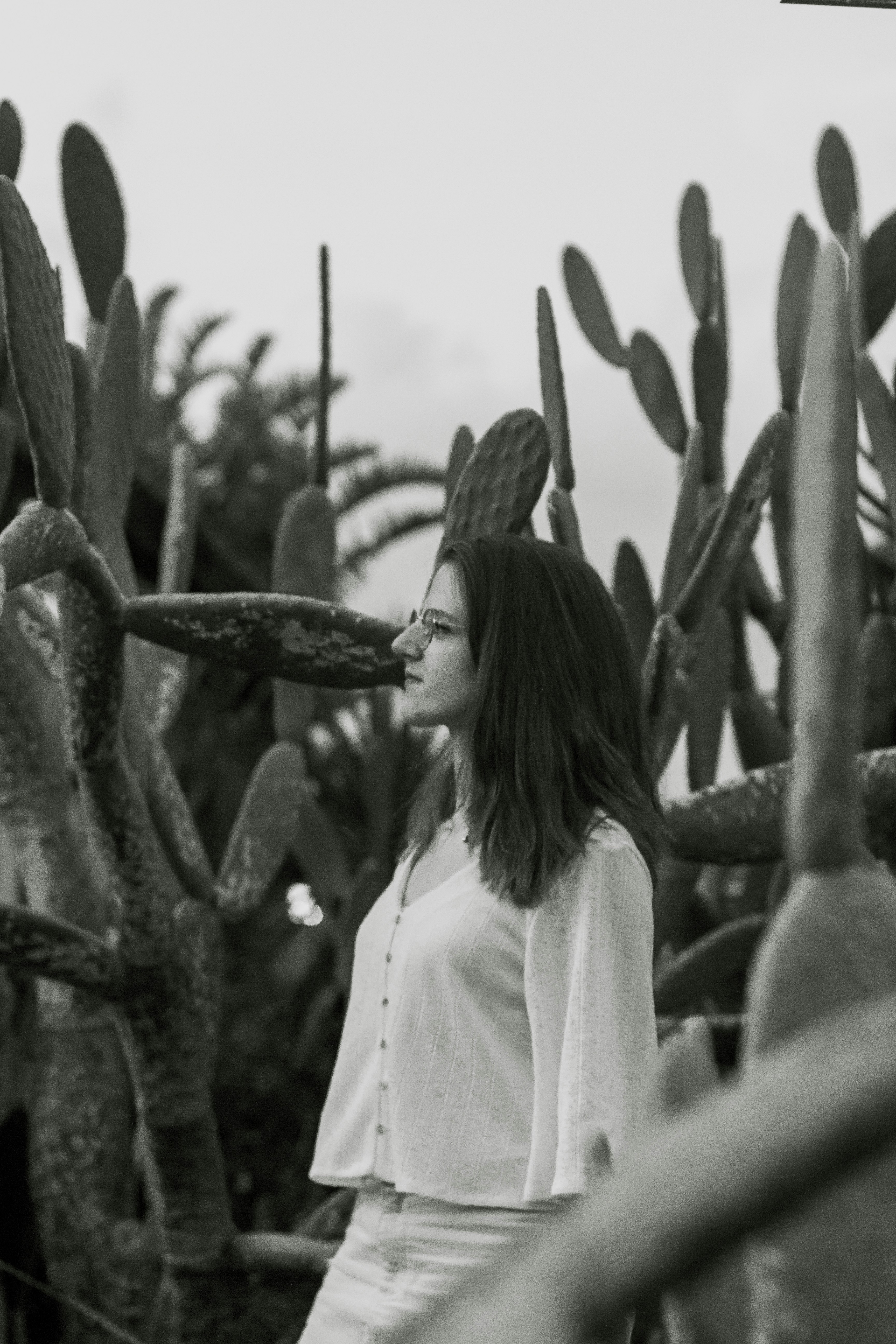 grayscale photo of woman standing near cactus plant